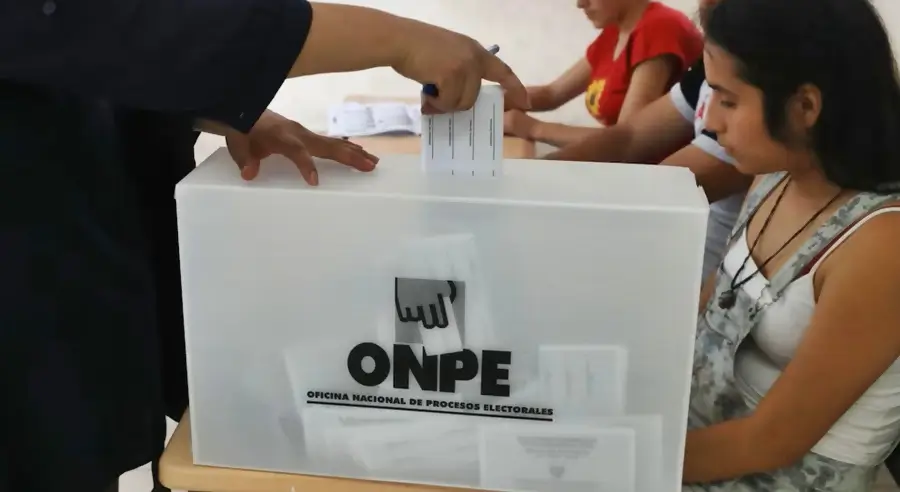 personas sentadas anotando mientras se ve la mano de una persona emitiendo su voto