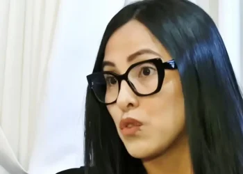 Mujer de cabello negro y gafas oscuras observando un documento en un ambiente interior