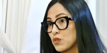 Mujer de cabello negro y gafas oscuras observando un documento en un ambiente interior