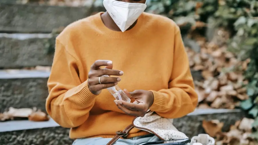 una persona protegiendose con mascarilla mientras en sus manos tiene un frasco