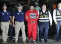 Detenido con uniforme rojo escoltado por agentes de INTERPOL y Policía Nacional del Perú durante operativo nocturno.