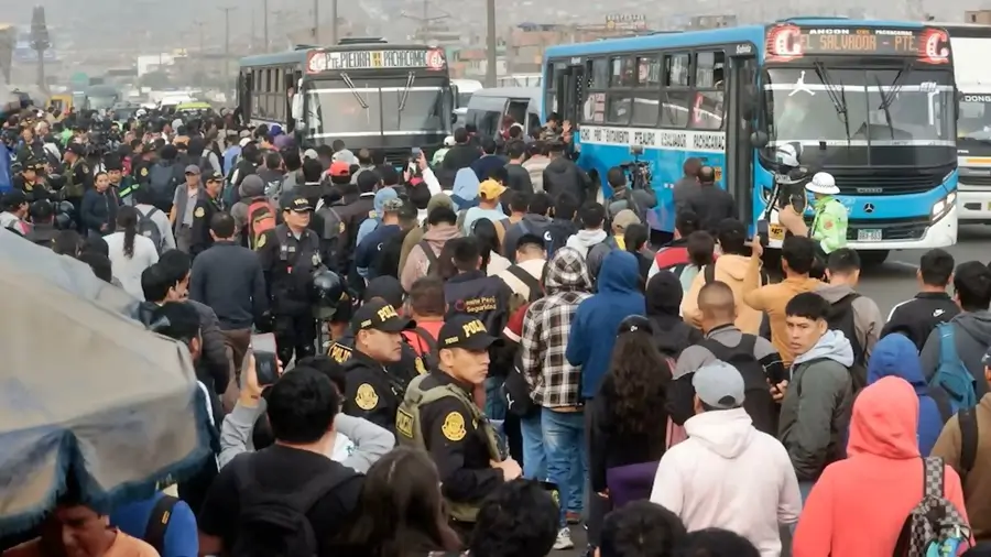 Multitud de personas y policías se concentran en una vía bloqueada por buses durante una protesta de transportistas.