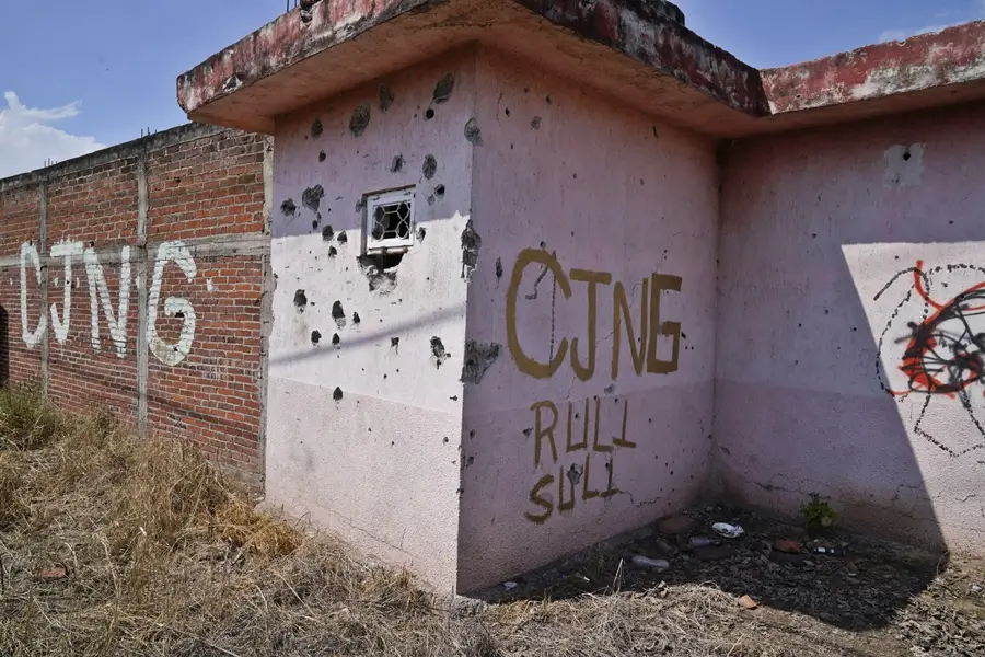 Fachada de vivienda con múltiples impactos de bala y grafiti del CJNG en un muro de México.
