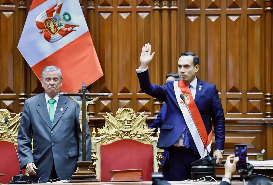 Hombre con banda presidencial levanta la mano durante una ceremonia oficial en el Congreso de la República del Perú, junto a otra autoridad, con la bandera peruana al fondo.