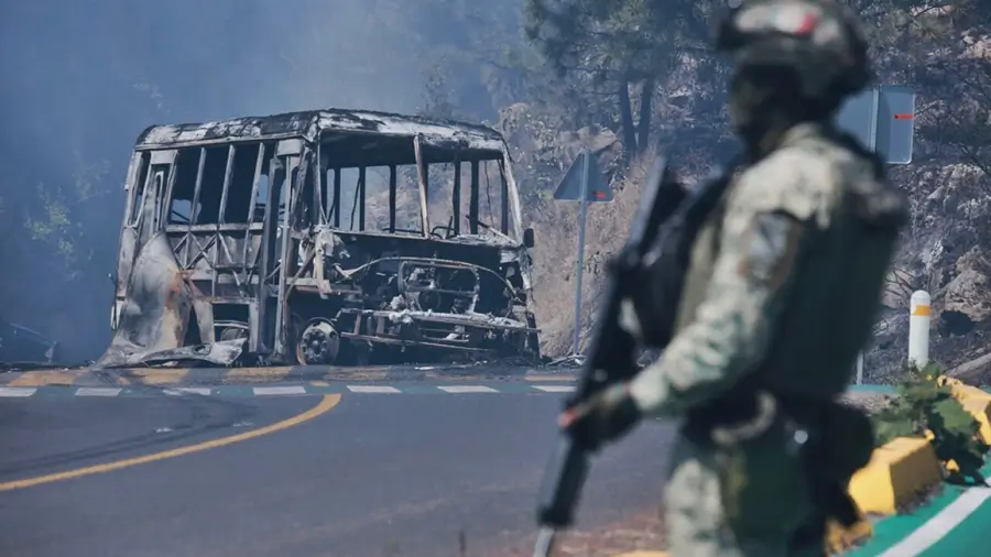 Autobús calcinado en carretera de México mientras un militar resguarda la zona tras hechos violentos vinculados a Rubén Oseguera Cervantes, alias ‘El Mencho’.