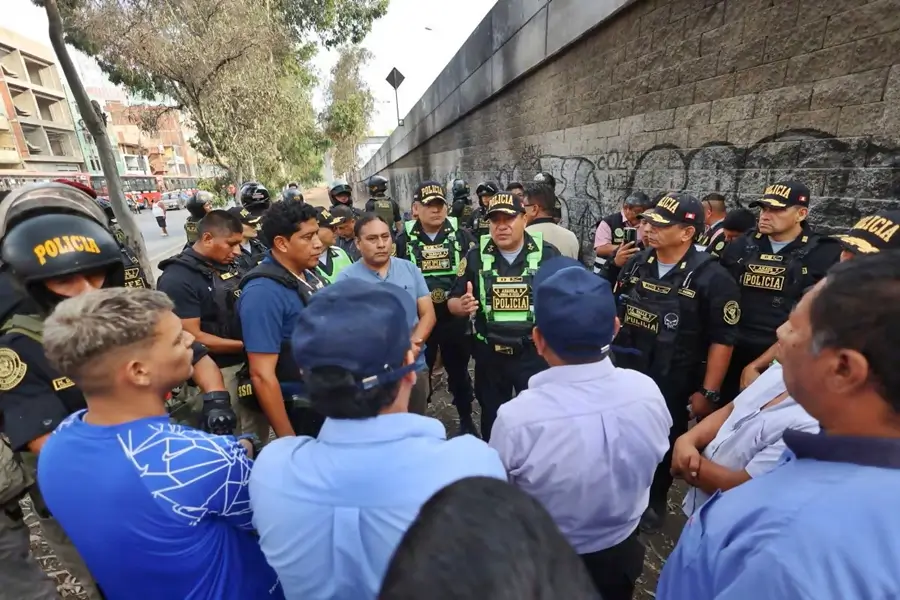 Policías con uniforme y civiles reunidos en calle urbana junto a pared con grafitis, en operativo de seguridad ciudadana.