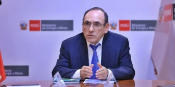 Representante del Ministerio de Energía y Minas del Perú durante reunión institucional, explicando políticas del sector energético en Perú, con bandera nacional y logos oficiales al fondo.