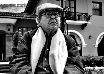 Retrato del escritor peruano Alfredo Bryce Echenique usando boina y lentes frente a una casona colonial.