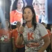 Keiko Fujimori hablando con micrófono en un mitin político; viste una camiseta blanca con el logo naranja de Fuerza Popular y de fondo se ve una pantalla gigante con su propia imagen.