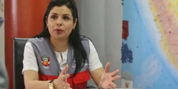 Funcionaria peruana sentada en una mesa de oficina, gesticulando mientras habla, con un mapa del Perú al fondo.
