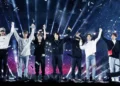 Integrantes de la banda K-pop BTS saludando juntos con los brazos arriba en pleno concierto en vivo