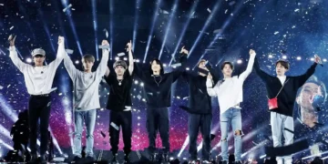 Integrantes de la banda K-pop BTS saludando juntos con los brazos arriba en pleno concierto en vivo