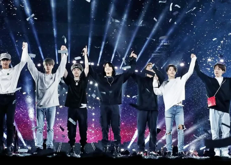 Integrantes de la banda K-pop BTS saludando juntos con los brazos arriba en pleno concierto en vivo
