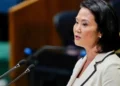 Keiko Fujimori con chaqueta blanca hablando frente a dos micrófonos en un podio durante un evento político.