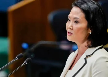 Keiko Fujimori con chaqueta blanca hablando frente a dos micrófonos en un podio durante un evento político.