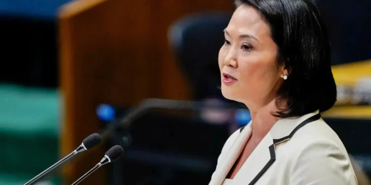 Keiko Fujimori con chaqueta blanca hablando frente a dos micrófonos en un podio durante un evento político.