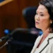 Keiko Fujimori con chaqueta blanca hablando frente a dos micrófonos en un podio durante un evento político.