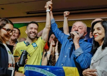 Lula da Silva habla por micrófono con el brazo en alto junto a seguidores con la bandera de Brasil.
