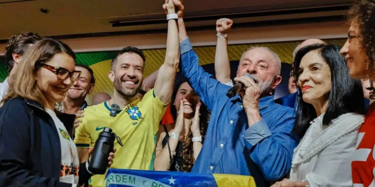 Lula da Silva habla por micrófono con el brazo en alto junto a seguidores con la bandera de Brasil.