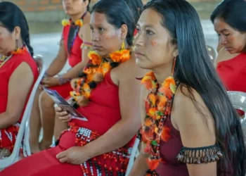 Mujeres awajún con trajes típicos y coloridos collares participando en una reunión oficial.