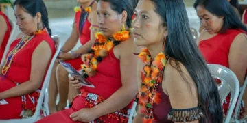 Mujeres awajún con trajes típicos y coloridos collares participando en una reunión oficial.
