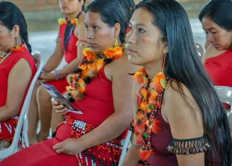 Mujeres awajún con trajes típicos y coloridos collares participando en una reunión oficial.